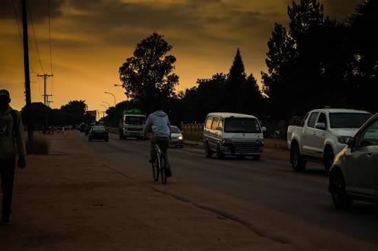 Commuters, minibuses and a cyclist on a Mogoditshane road at dusk